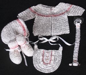 WHITE RAYON WITH TINY PINK EMBROIDERED FLOWERS.  SET INCLUDES; BOOTIES, HAT, PACIFIER HOLDER, BIB, SWEATER.