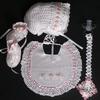 WHITE RAYON WITH EMBROIDERED PINK FLOWER EMBELISHMENT. SET INCLUDES BOOTIES, HAT, PACIFIER HOLDER, BIB.