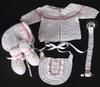 WHITE RAYON WITH TINY PINK EMBROIDERED FLOWERS. SET INCLUDES; BOOTIES, HAT, PACIFIER HOLDER, BIB, SWEATER.